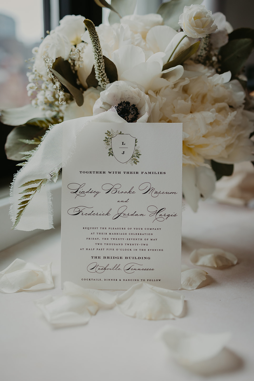 Wedding invitation on top of white flower petals, leaning against bouquet