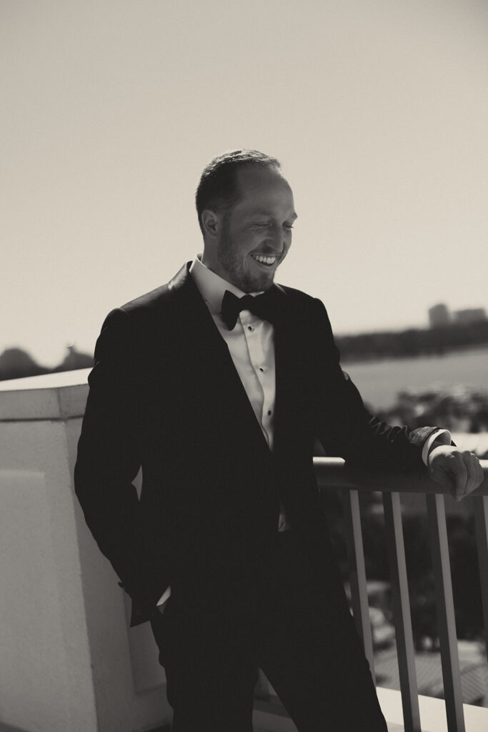 Groom smiles wearing custom Richards Bespoke suit while standing on poolside balcony