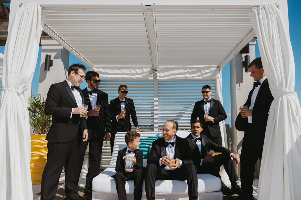 Groomsmen and ring bearer sit poolside in their tuxedos in Miramar Beach wedding