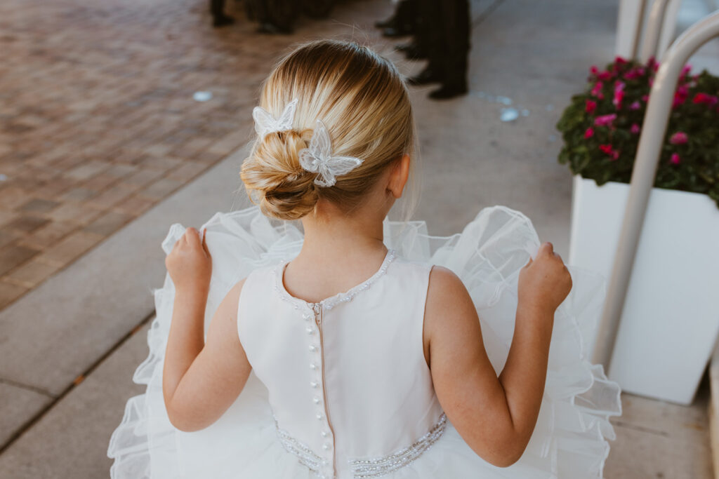 Flower girl plays with her tutu dress while wearing butterfly clips in her hair