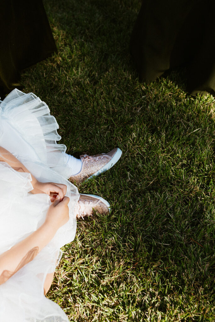 Flower girl's sparkly pink sneakers sparkle in the sunlight while she sits in the grass
