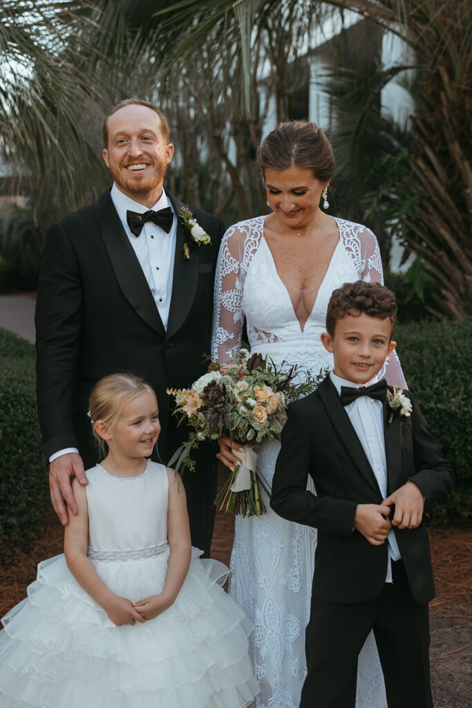 Bride and groom smile down at ring bearer and flower girl in Miramar Beach destination wedding
