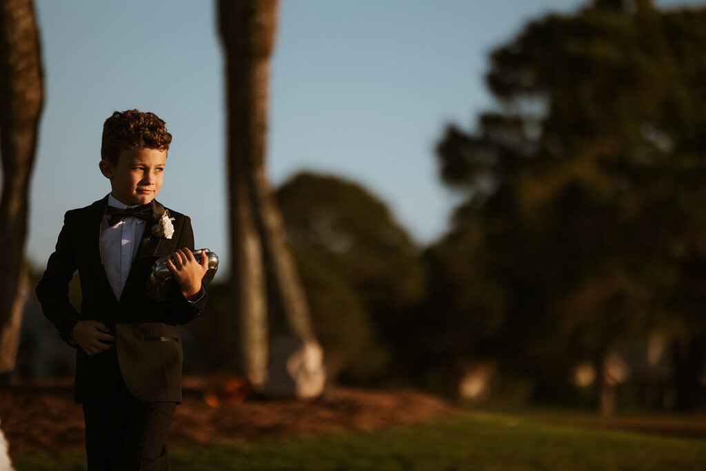 Ring bearer walks down the aisle while golden hour sun hits his face