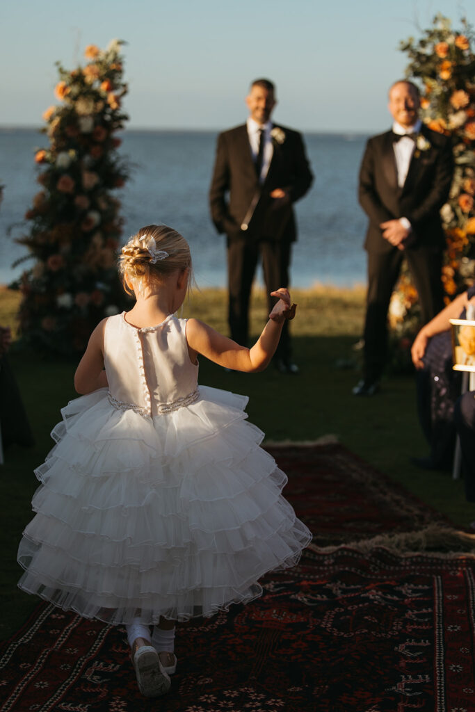 Groom smiles as flower girl comes down the aisle