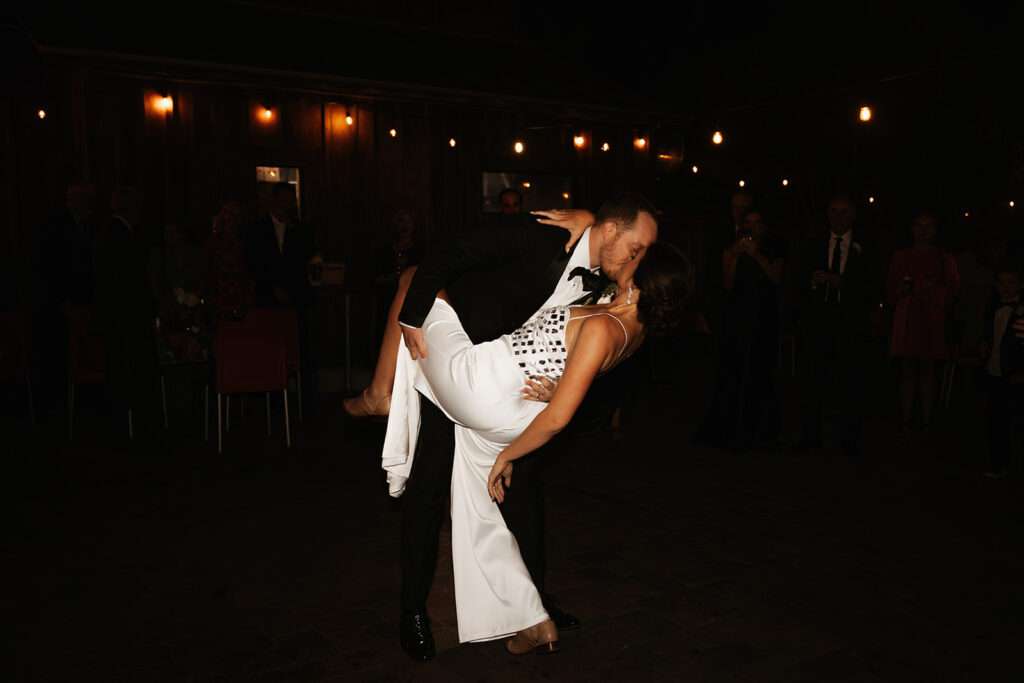 Groom dips bride wearing white jumpsuit in first dance