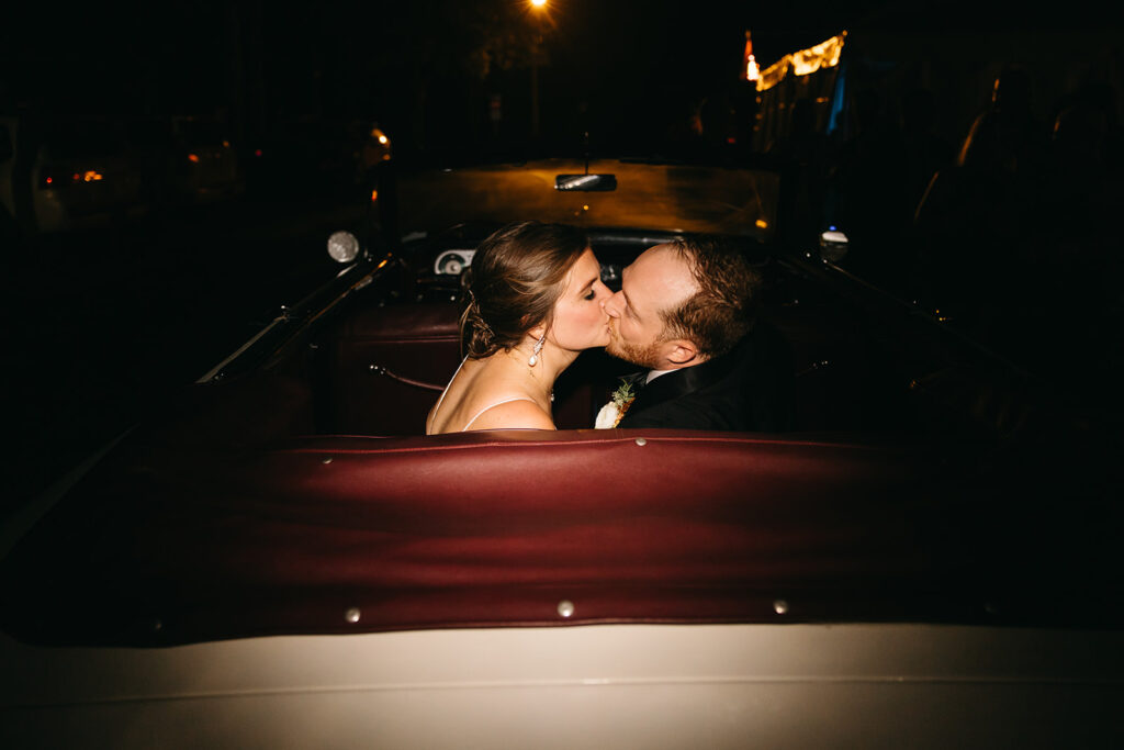 Bride and groom share kiss in back of vintage convertible