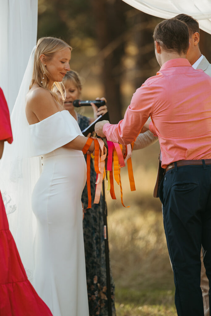 Wedding guest tells bride and groom what he loves about them as he places ribbon on bride's wrists.