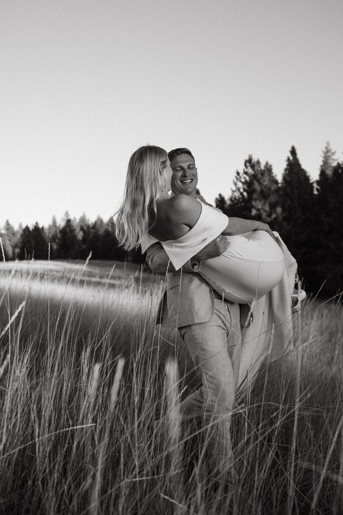 Groom carries expecting bride through prairie grass in Idaho destination wedding