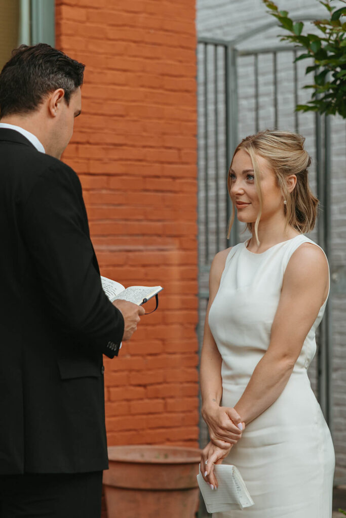 Bride looks adoringly at groom as he reads his vows in courthouse wedding