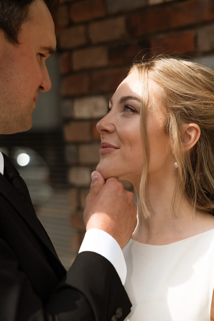 Groom cups bride's chin in his hand in gentle embrace