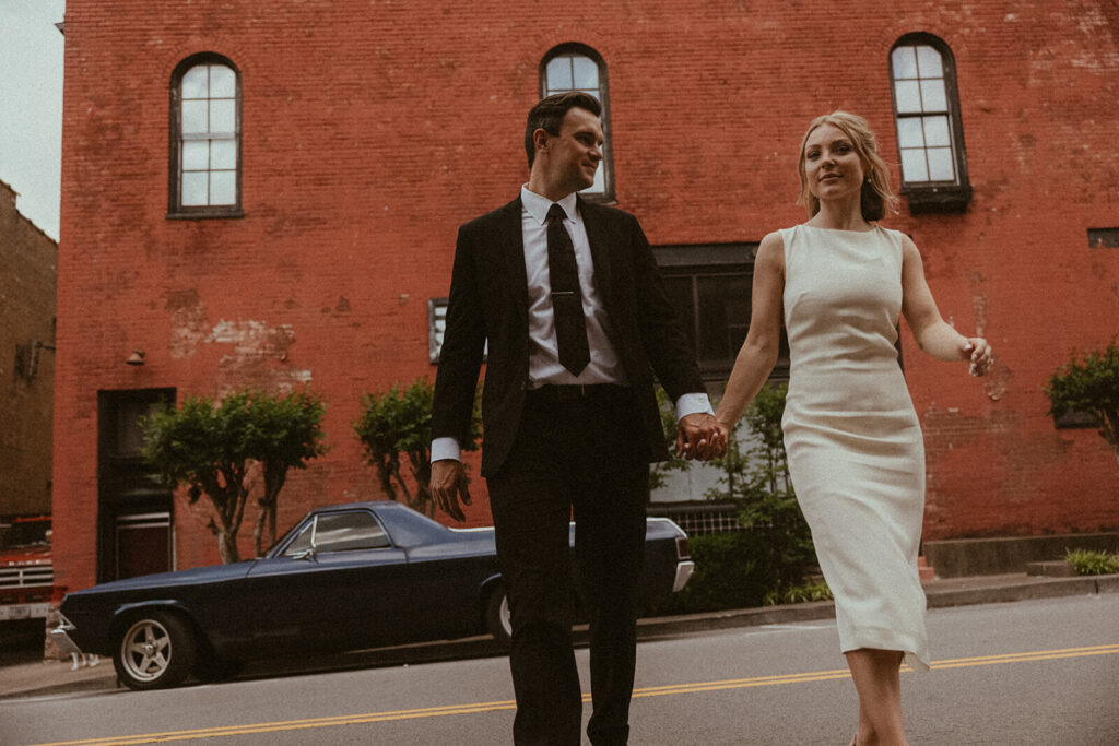 Bride and groom walk towards camera with vintage car in the background