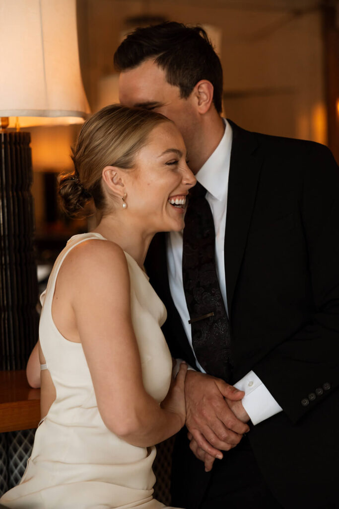 Bride laughs as groom whispers something in her ear