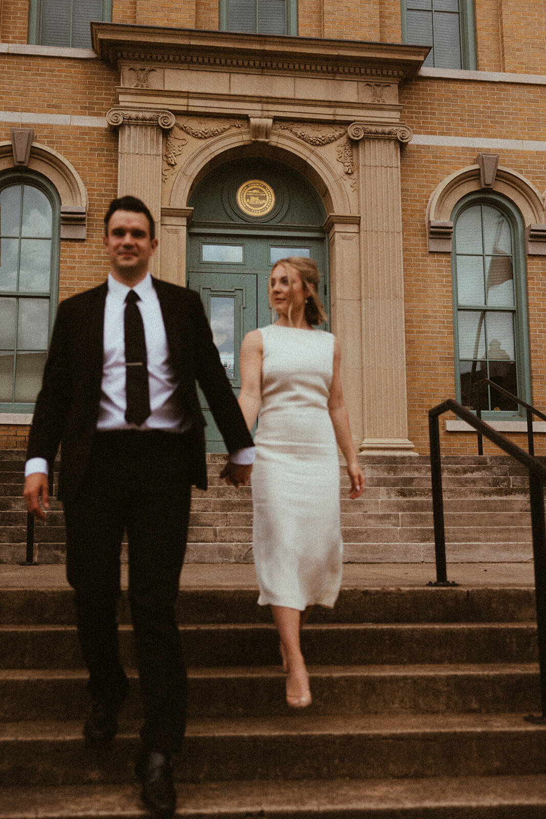 Bride and groom come down the steps of elegant courthouse wedding.