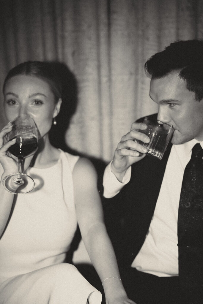 Groom sips old fashioned and bride sips glass of red wine at courthouse wedding after party