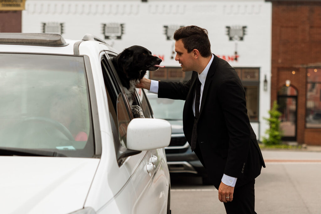 Groom pets his dog greeting him out the window of the car