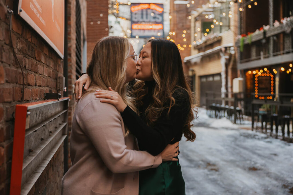 Couple kisses in Printer's Alley in Nashville during snowy destination engagement session.