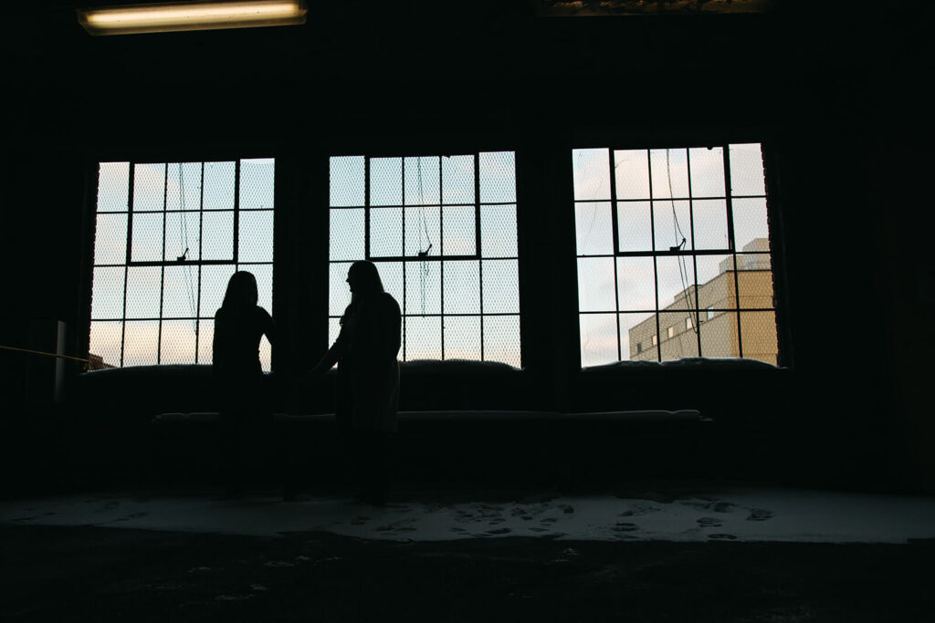 Couple is silhouetted outside of empty warehouse in downtown Nashville engagement photoshoot.