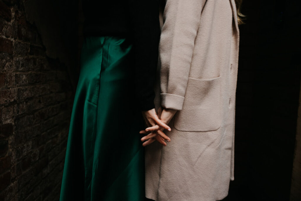 Woman in emerald green skirt and woman in beige overcoat hold hands.