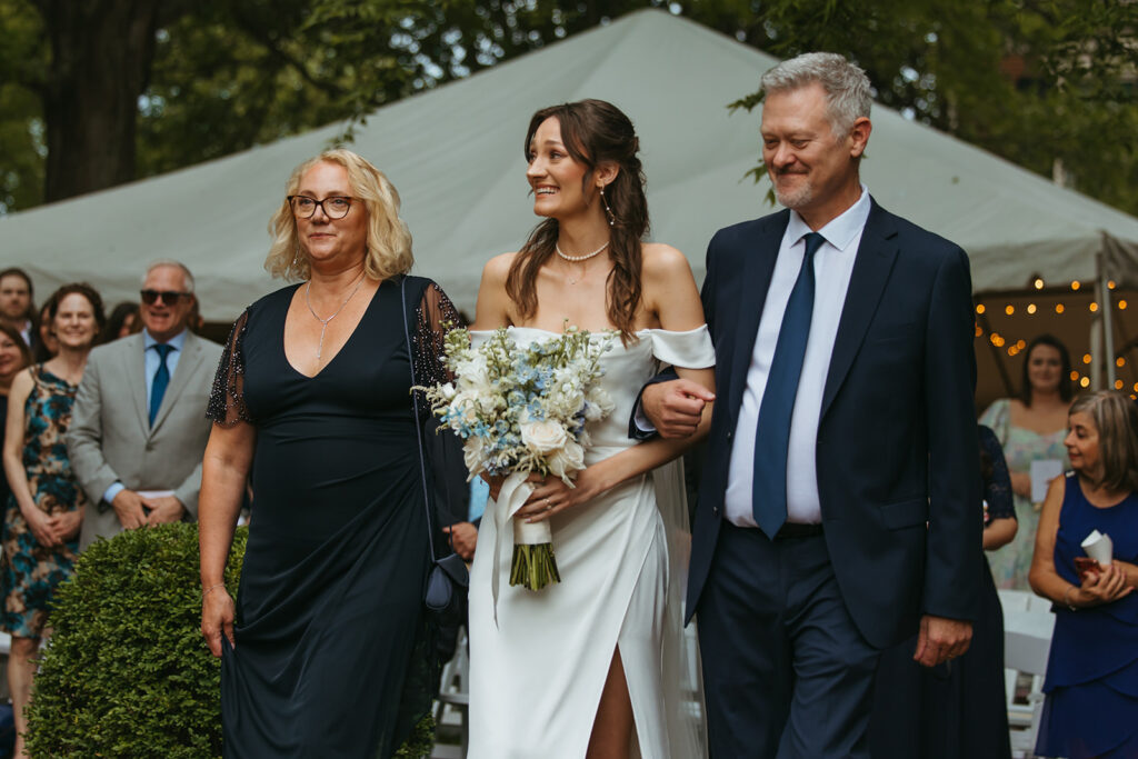 Bride looks at groom as she walks up the aisle towards him, with her parents on each side of her