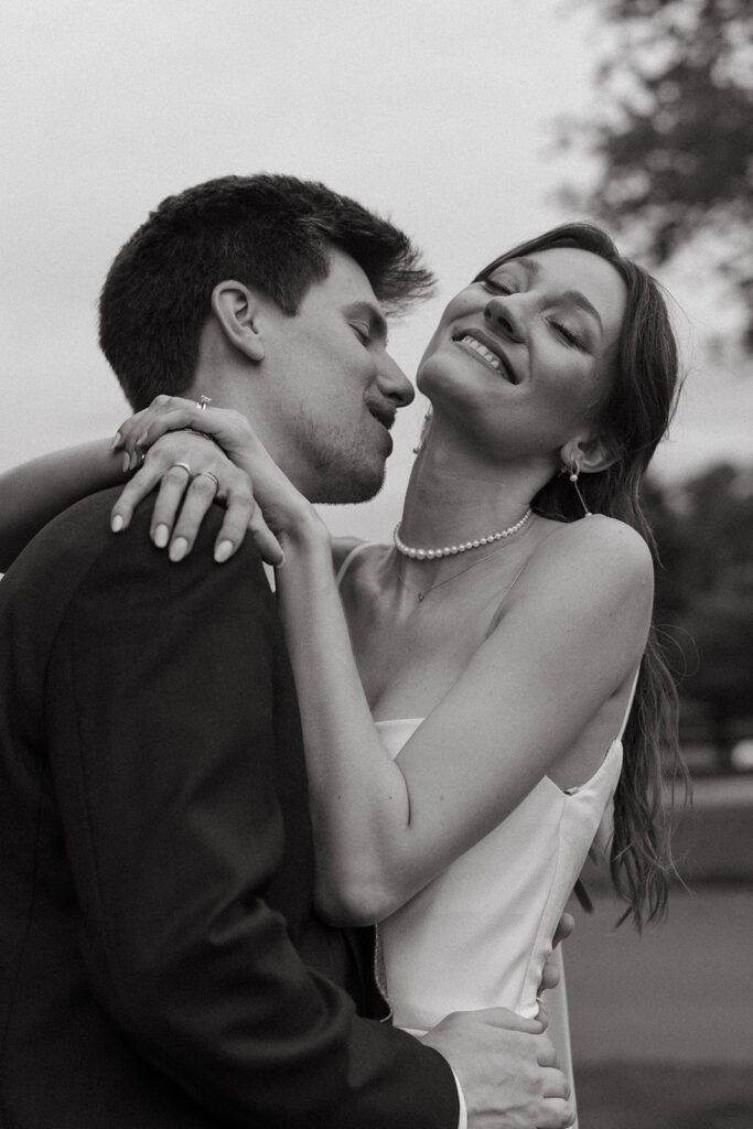 Groom kisses bride's neck while she smiles towards the sky in documentary style wedding photos