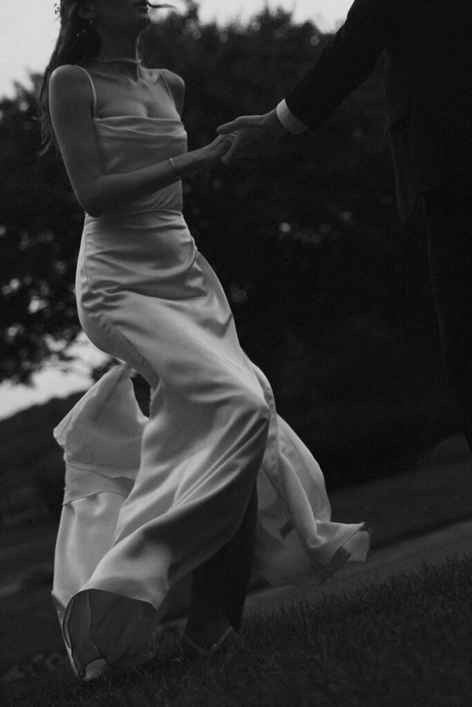 Groom holds bride's hand as she dances around in the grass in documentary style wedding photos