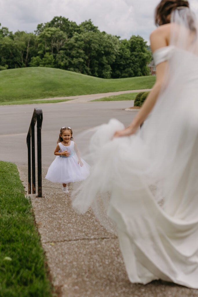 Bride leans down to give flower girl a hug as she comes up the stairs