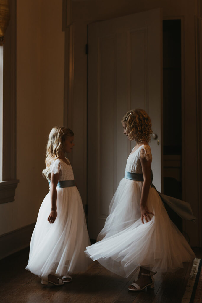 Flower girls show off their dresses for each other in documentary style wedding photos