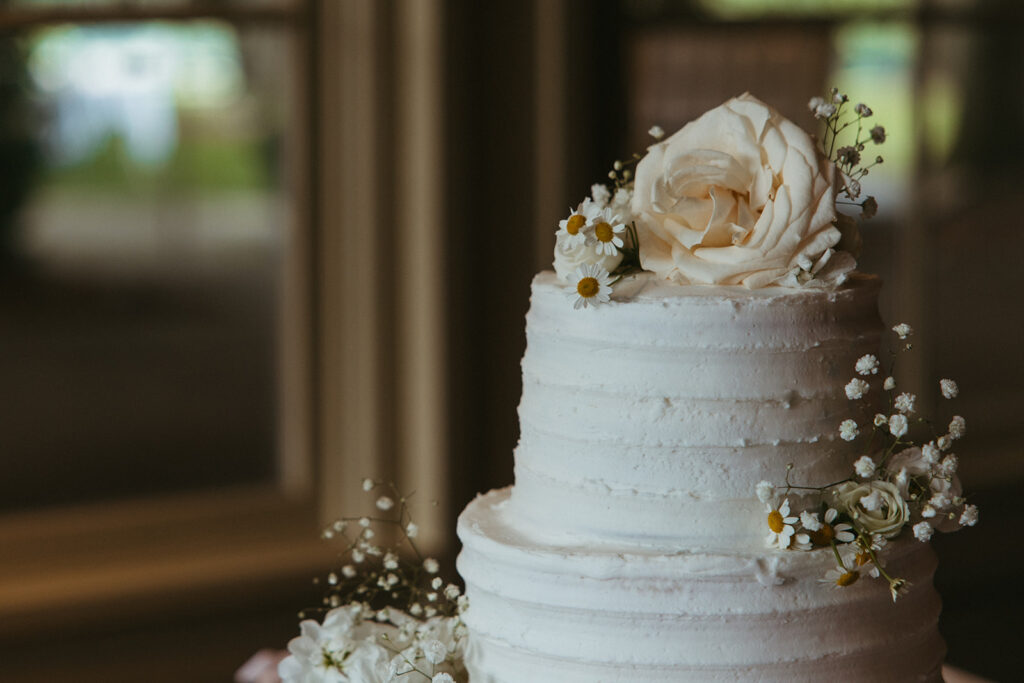 Elegant, simple wedding cake adorned with one peach rose and little daisies and baby's breath