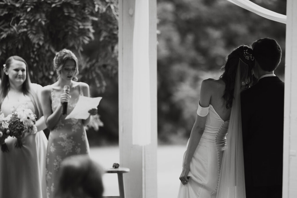 Bride leans on groom as maid of honor reads prayer during documentary style wedding ceremony