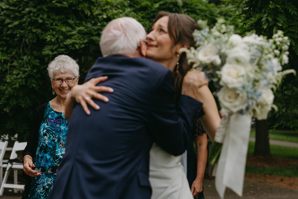 Bride hugs grandpa in emotional embrace as grandma smiles on in the background