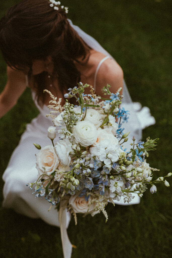 Bride crouches down on the lush grass while holding onto her beautiful bridal bouquet