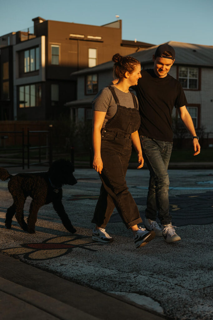 Man and woman walk in Nashville golden hour as their poodle trails along behind them