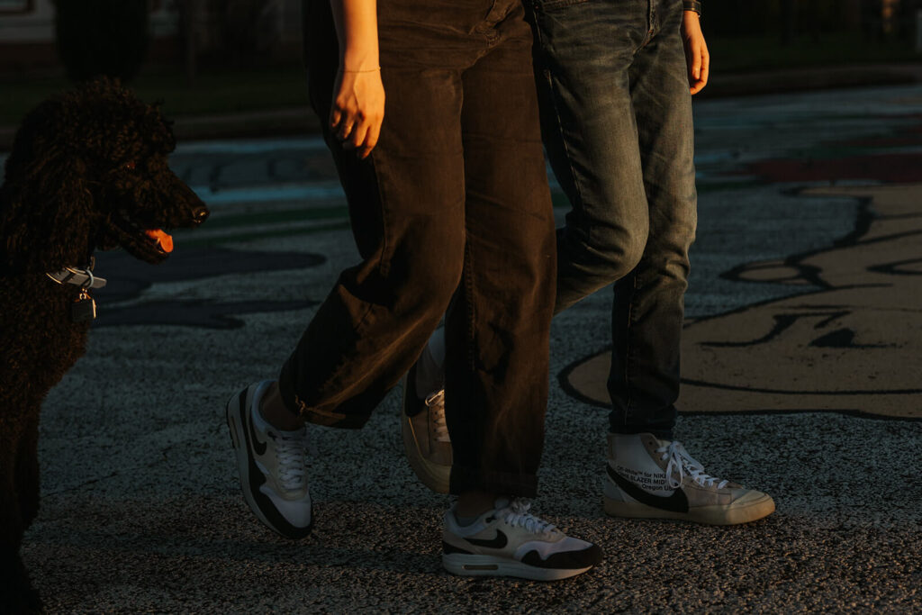 Engaged couple walks hand in hand as dog trails behind