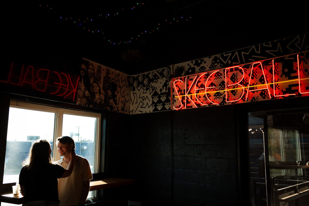 Engagement photographer captures couple under neon Skeeball sign