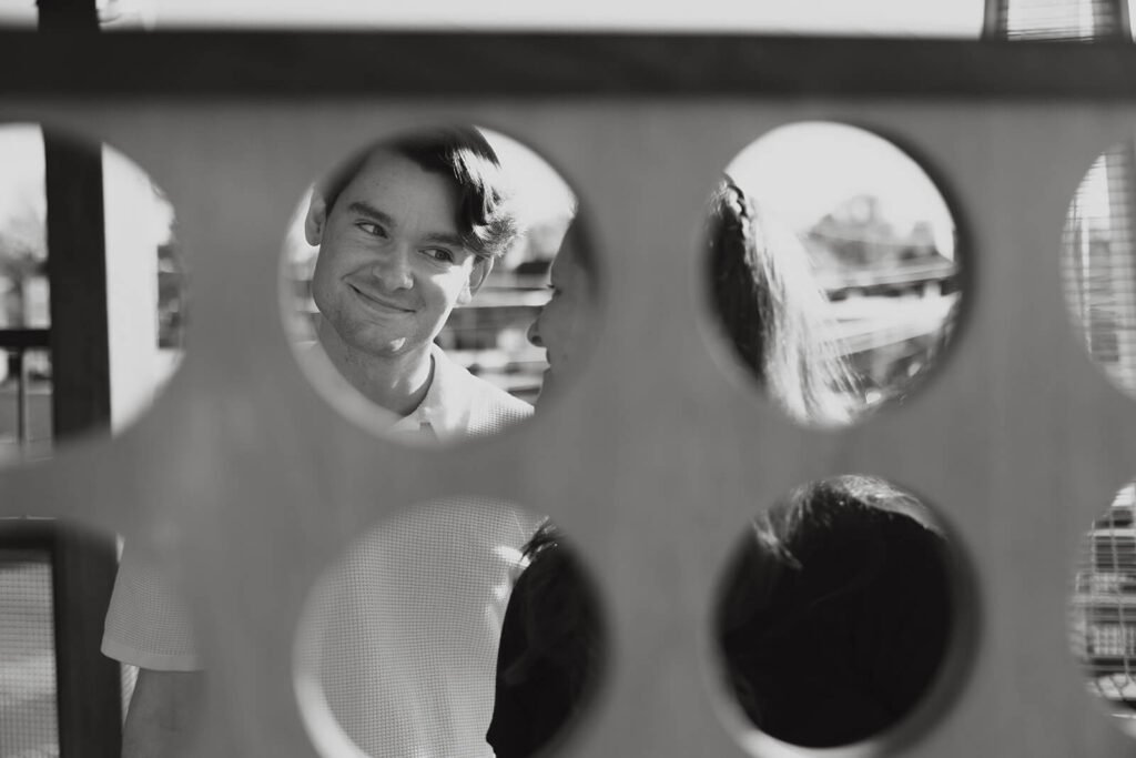 Man looks at woman with cheeky grin as engagement photographer captures them through Connect Four game