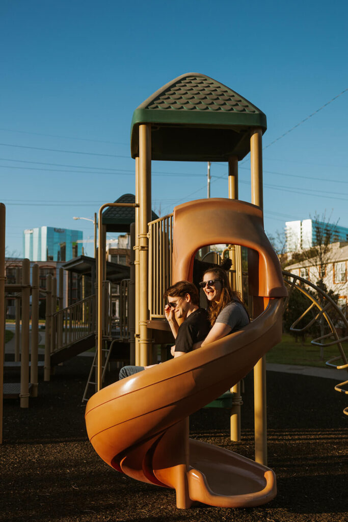 Engagement photographer captures couple going down the slide at playground together