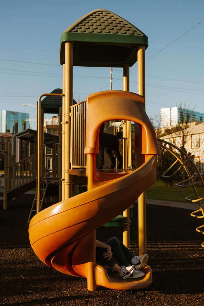 Engaged couple comes down orange slide on playground