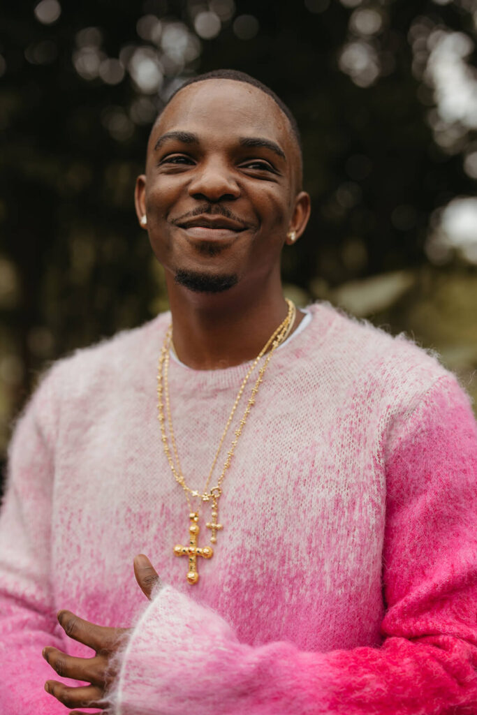 Man in fluffy pink sweater smiles off into the distance