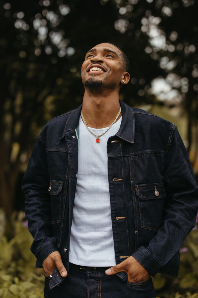 Man in white tee and dark denim jacket smiles looking up at the sky