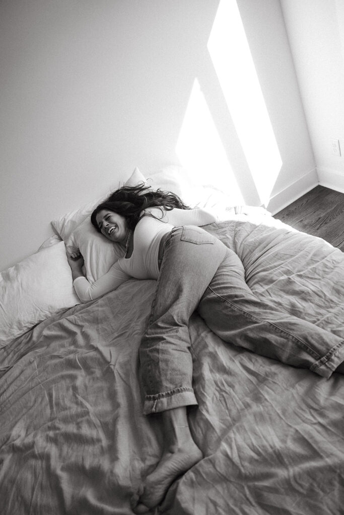 Woman wearing white tshirt and denim splays out on her bed 