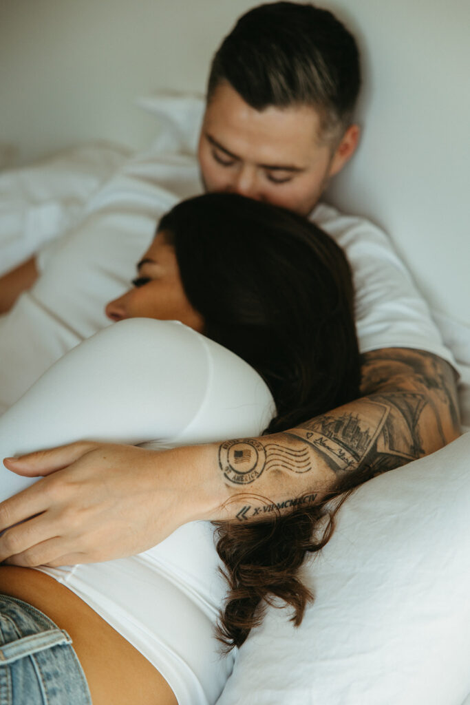 Man kisses top of fiance's head as they snuggle under the sheets