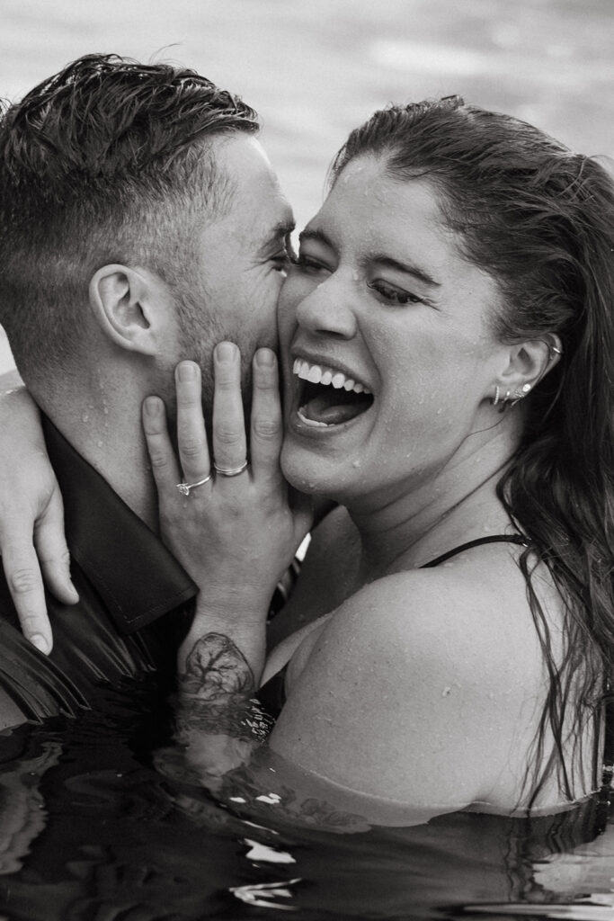 Woman laughs as her fiance whispers in her ear while they are floating in the pool