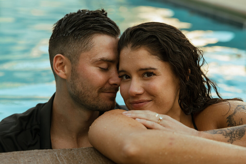 Man and woman smile in romantic engagement pool photoshoot