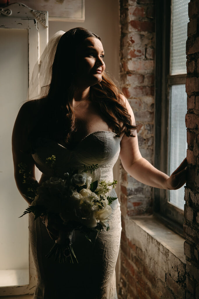 Bride stands in the natural light coming through the window of Emerald Union wedding venue 