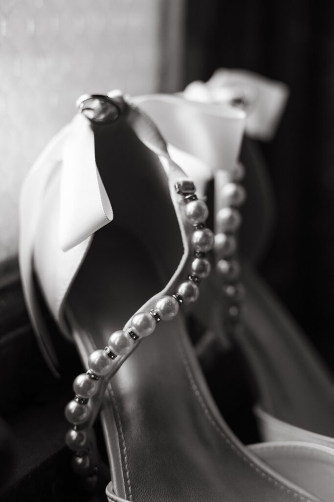 Bride's pearl adorned shoes with a bow on the back sit on the windowsill