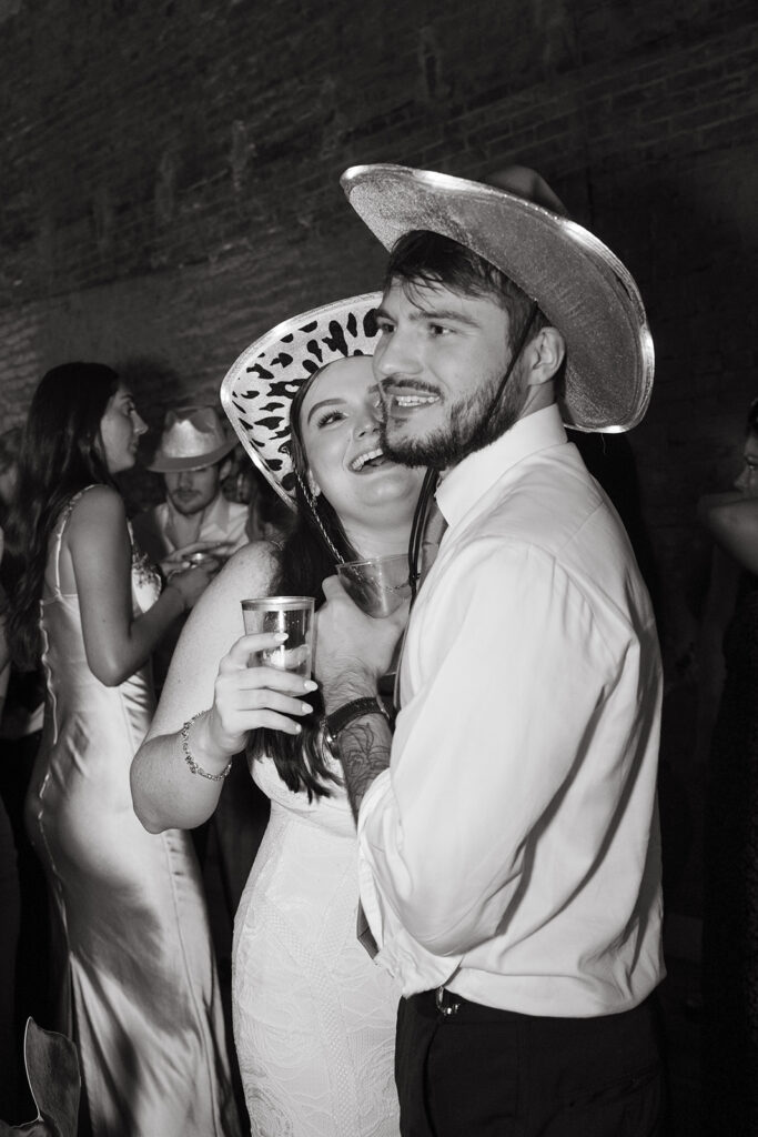 Bride and groom both wear cowboy hats as bride looks up at her husband