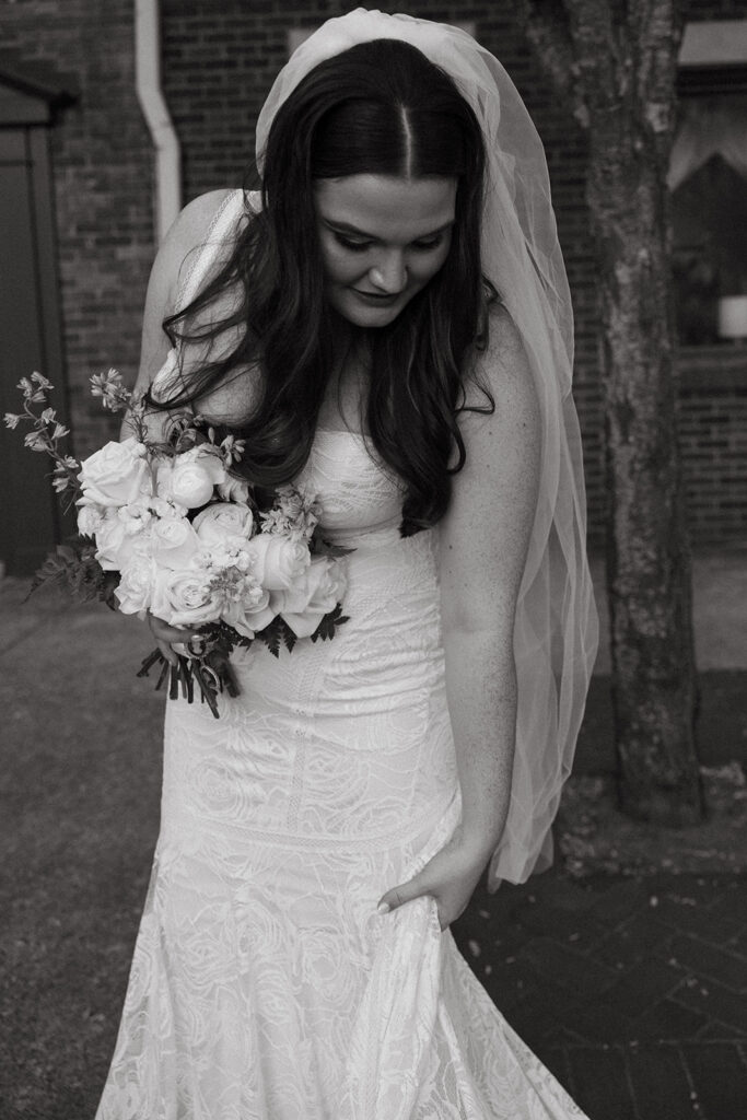 Elegant bride fixes her train while standing outside Emerald Union in Gallatin, Tennessee