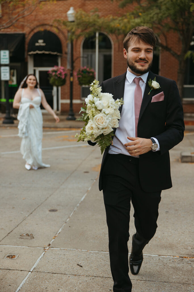 Bride follows after groom walking through the street with her bouquet