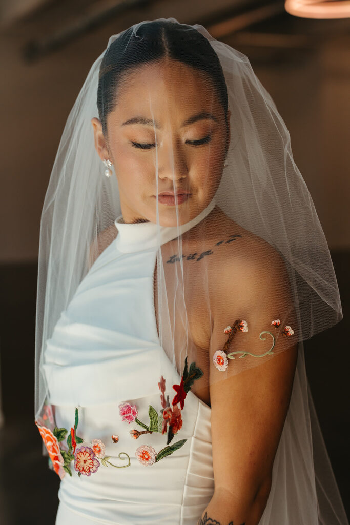 Bride looks down under the sheer cover of her Janesse Russel veil with hand-sewn flowers