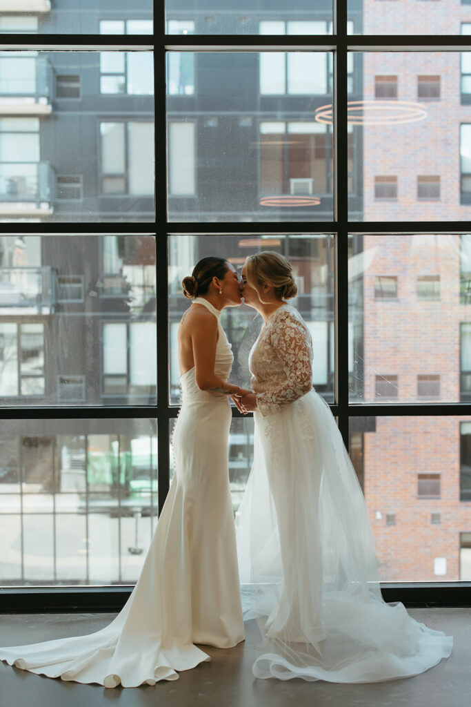 Brides kiss in front of open windows overlooking downtown Minneapolis cityscape